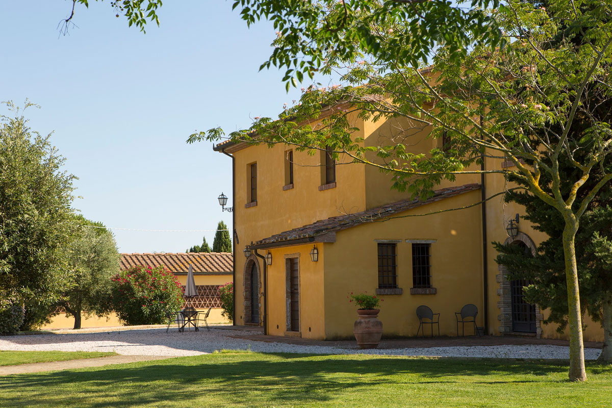 Exterior of the Aia Vecchia wine estate in Tuscany surrounded by gardens and olive trees.