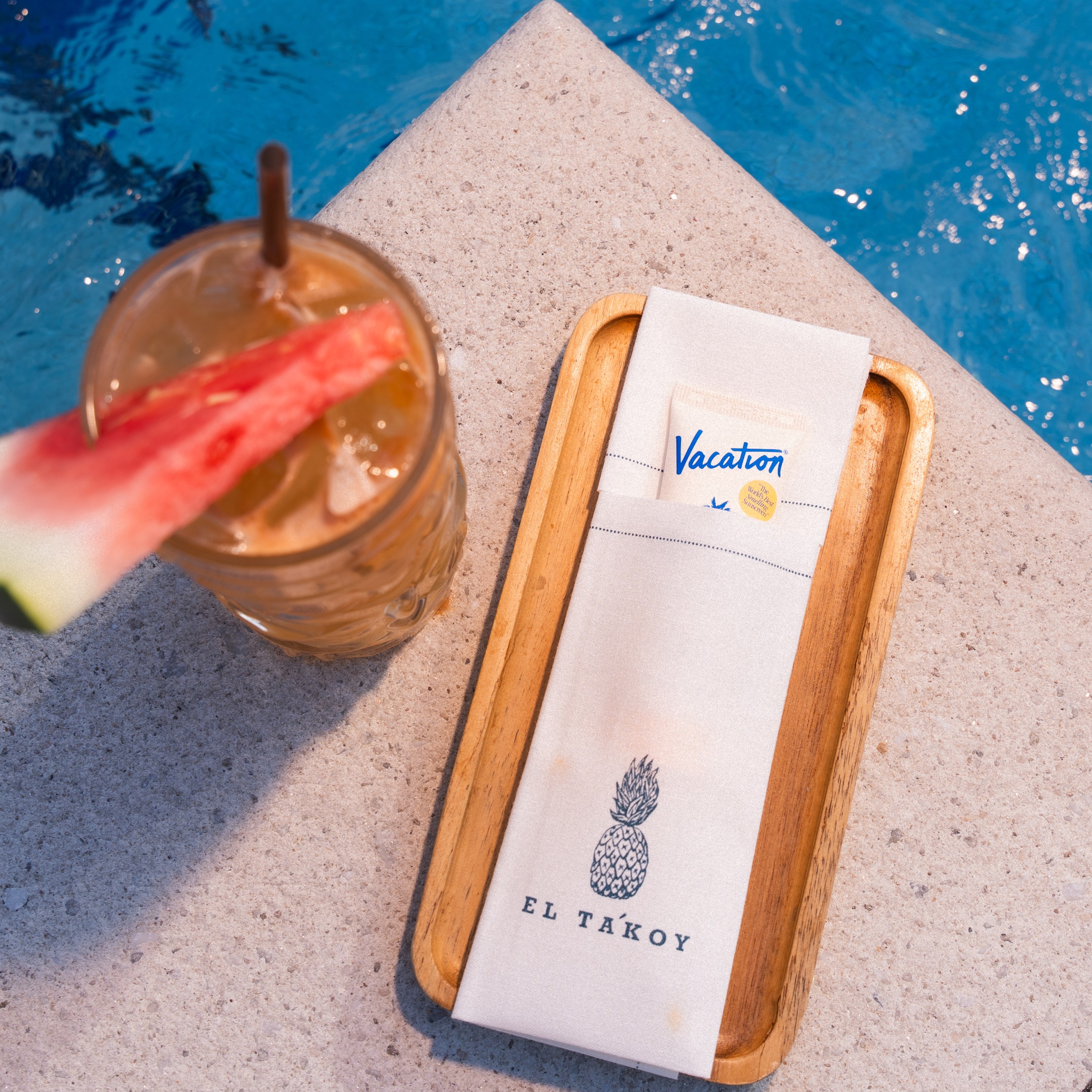 Overhead view of the Mana Breeze cocktail with watermelon garnish beside the pool at The Dominick hotel.