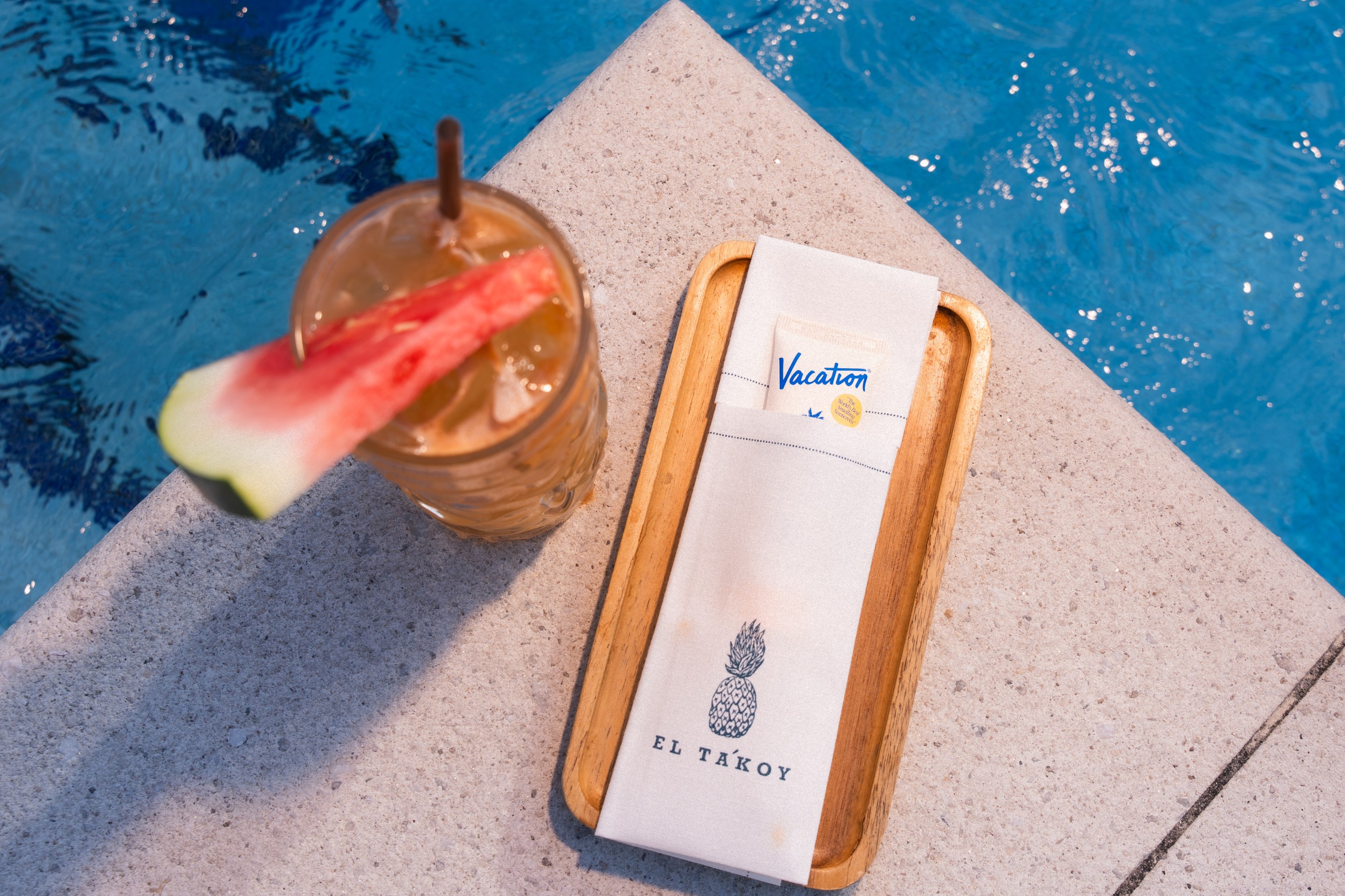Overhead view of the Mana Breeze cocktail with watermelon garnish beside the pool at The Dominick hotel.