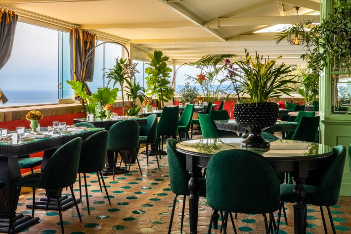 Interior of Euphoria restaurant in Taormina with green velvet chairs, tropical plants, and views of the Ionian Sea.