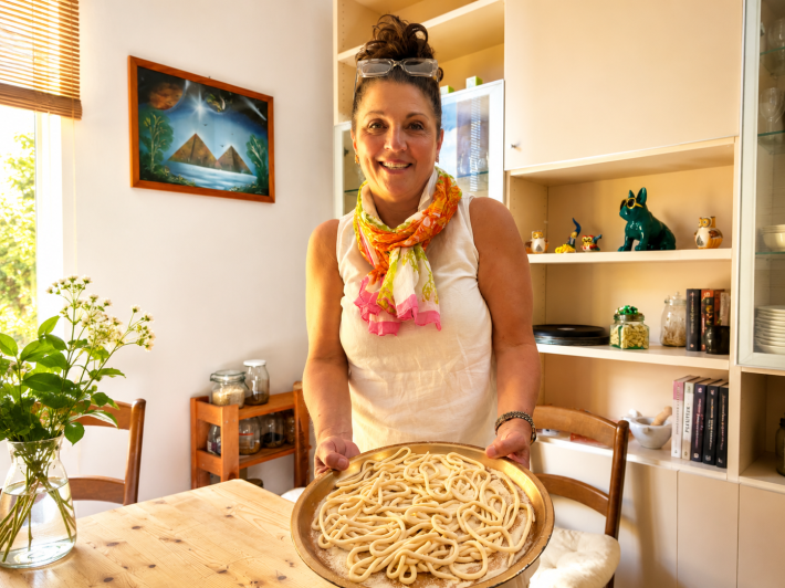 Mandi Casey holding a tray of homemade pici pasta during a cooking experience in Florence, Italy.