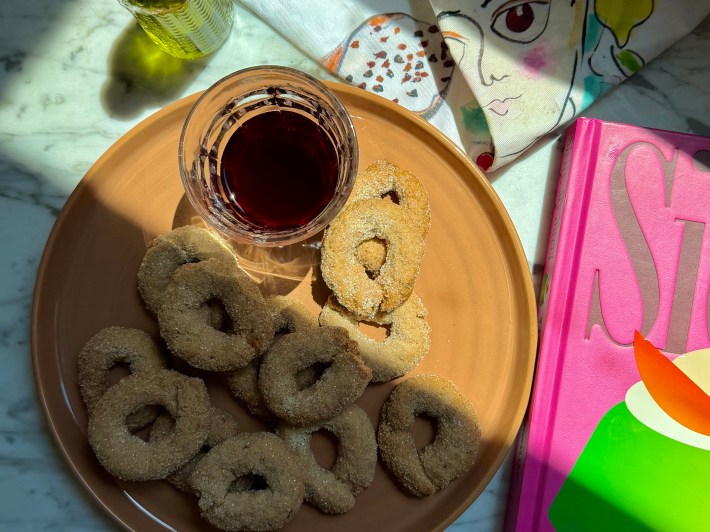 Traditional Sicilian biscotti al vino on a plate beside a glass of red wine.