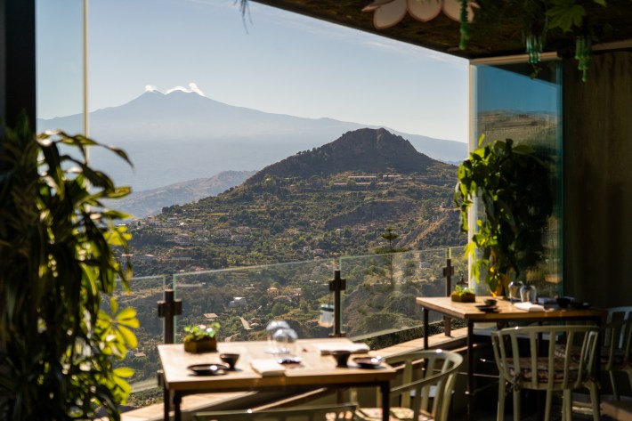 View of Mount Etna from Incanto restaurant in Taormina, Sicily, with dining tables overlooking the surrounding hills.