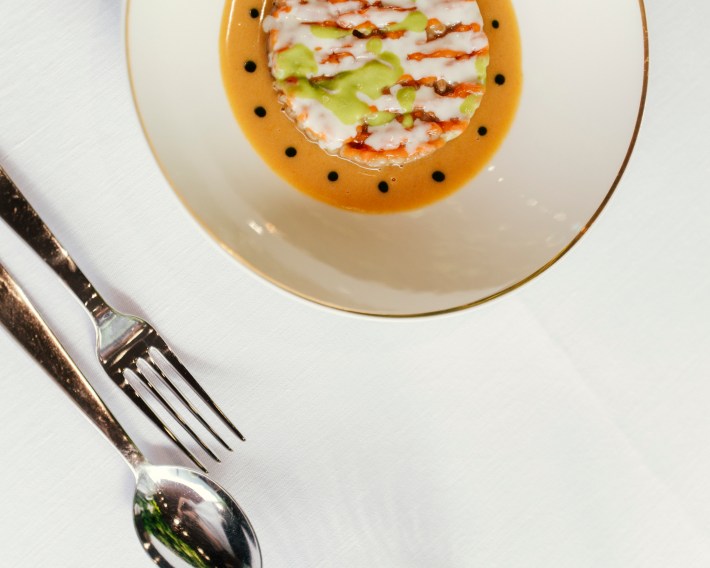 Trentino Barley “Orzotto” - An ancient grain prepared with speck, celery, carrots, and horseradish, served in a round bowl with a gold trim, next to silverware.