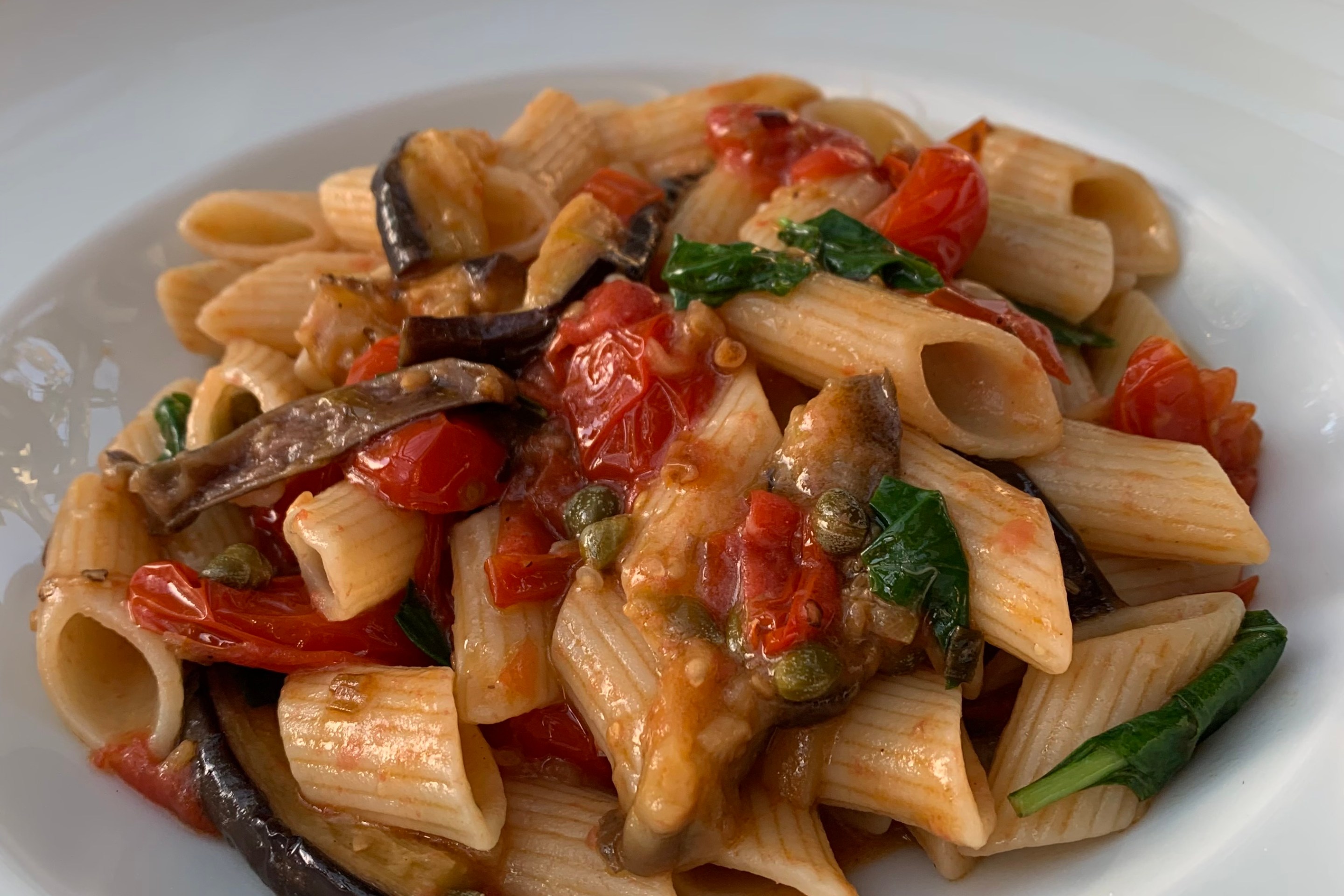 Penne pasta with sautéed eggplant, cherry tomatoes, capers, and fresh basil in a light tomato sauce.