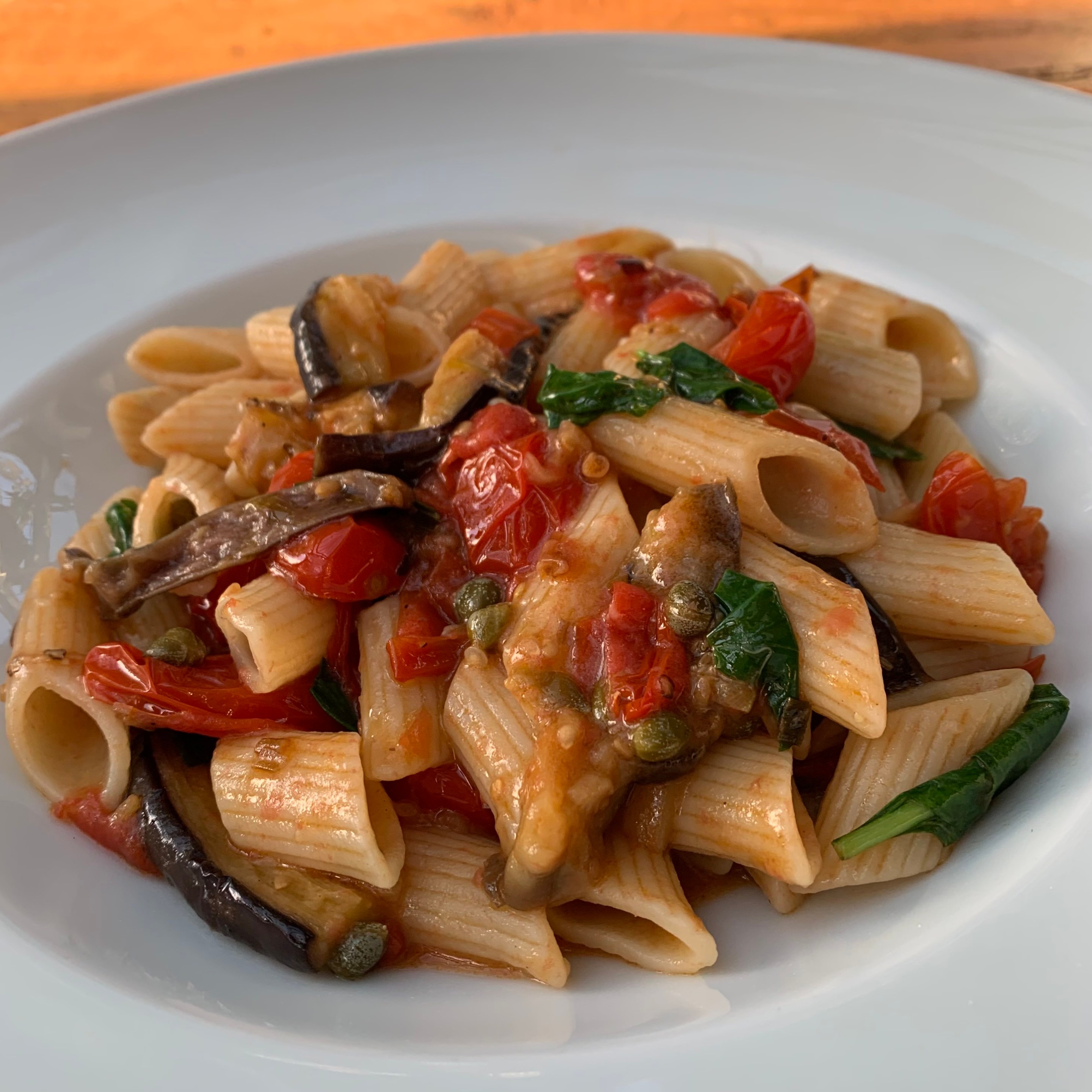 Penne pasta with sautéed eggplant, cherry tomatoes, capers, and fresh basil in a light tomato sauce.
