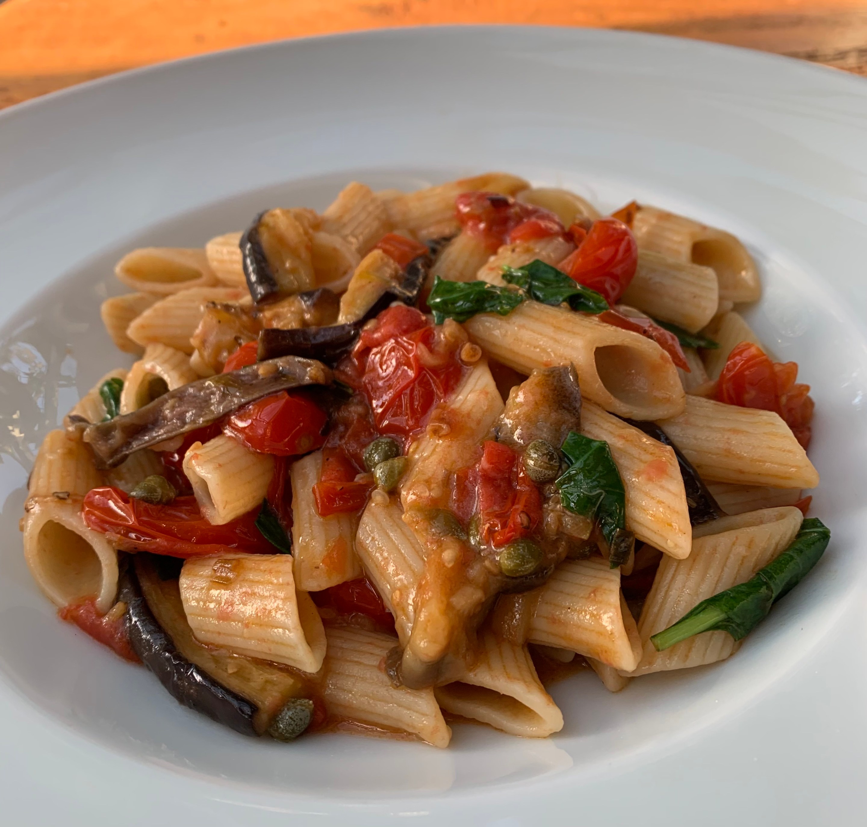Penne pasta with sautéed eggplant, cherry tomatoes, capers, and fresh basil in a light tomato sauce.