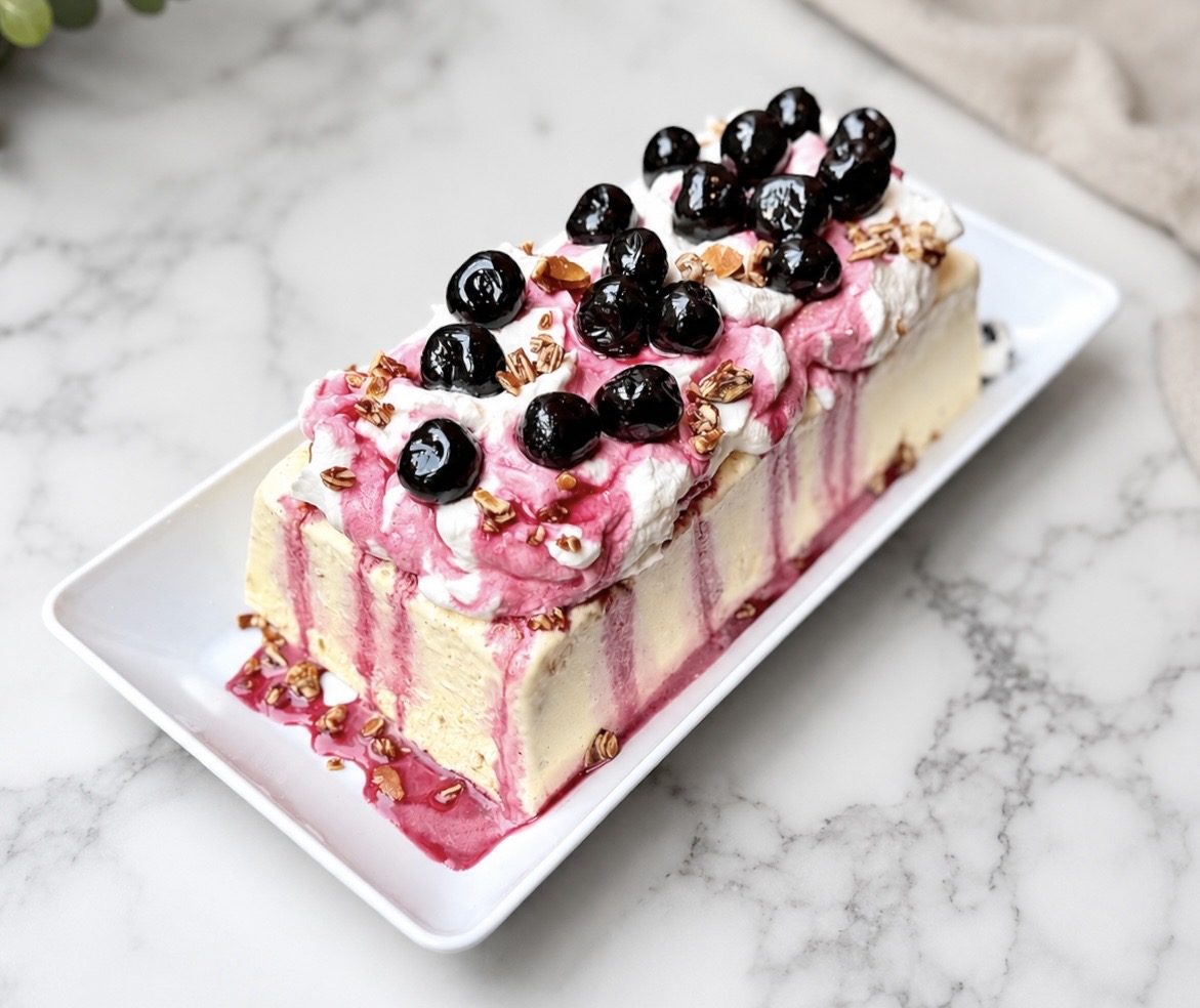 Almond semifreddo topped with whipped cream, almond brittle, and amarena cherries on a serving platter.
