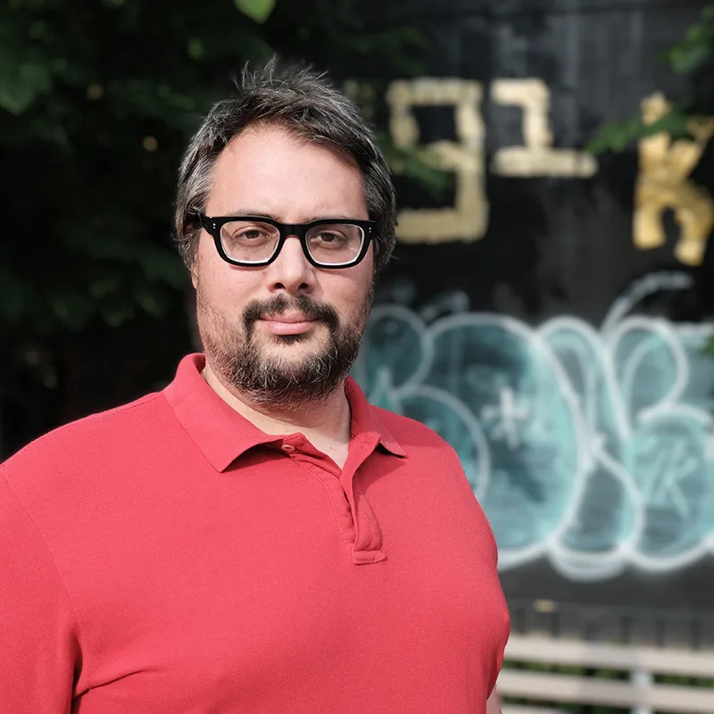 Bio pic of Ian MacAllen in a red shirt with glasses.