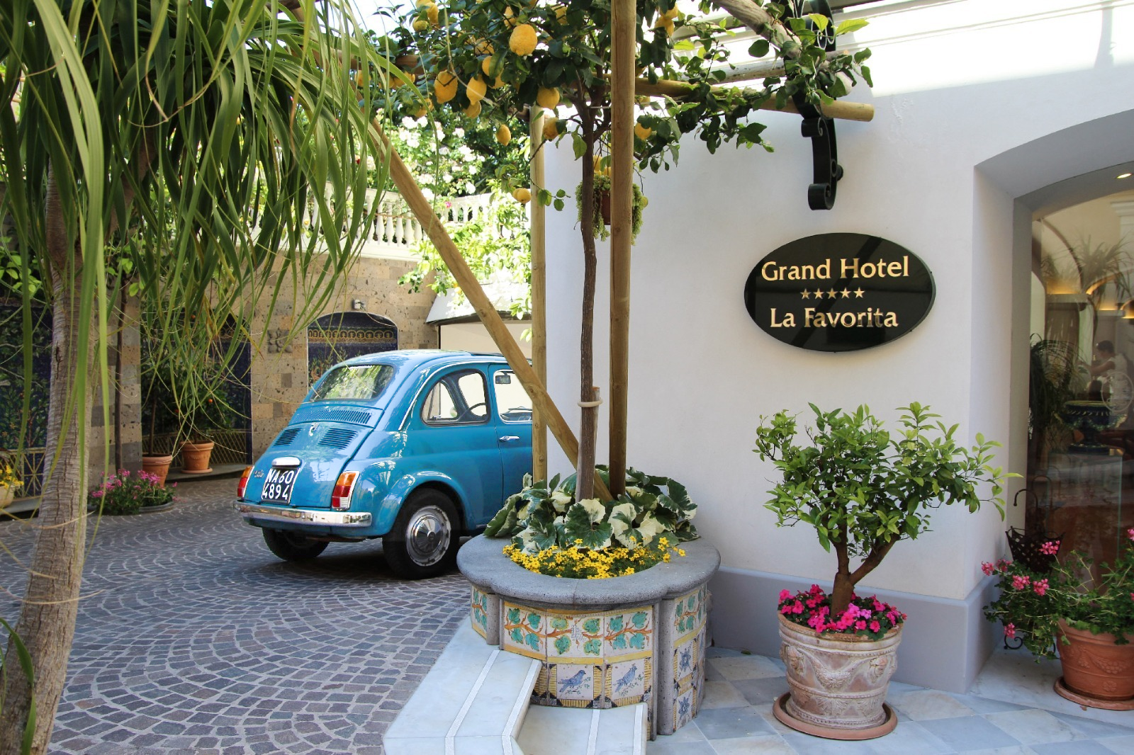 Entrance courtyard of Grand Hotel La Favorita with vintage Fiat and lemon trees.