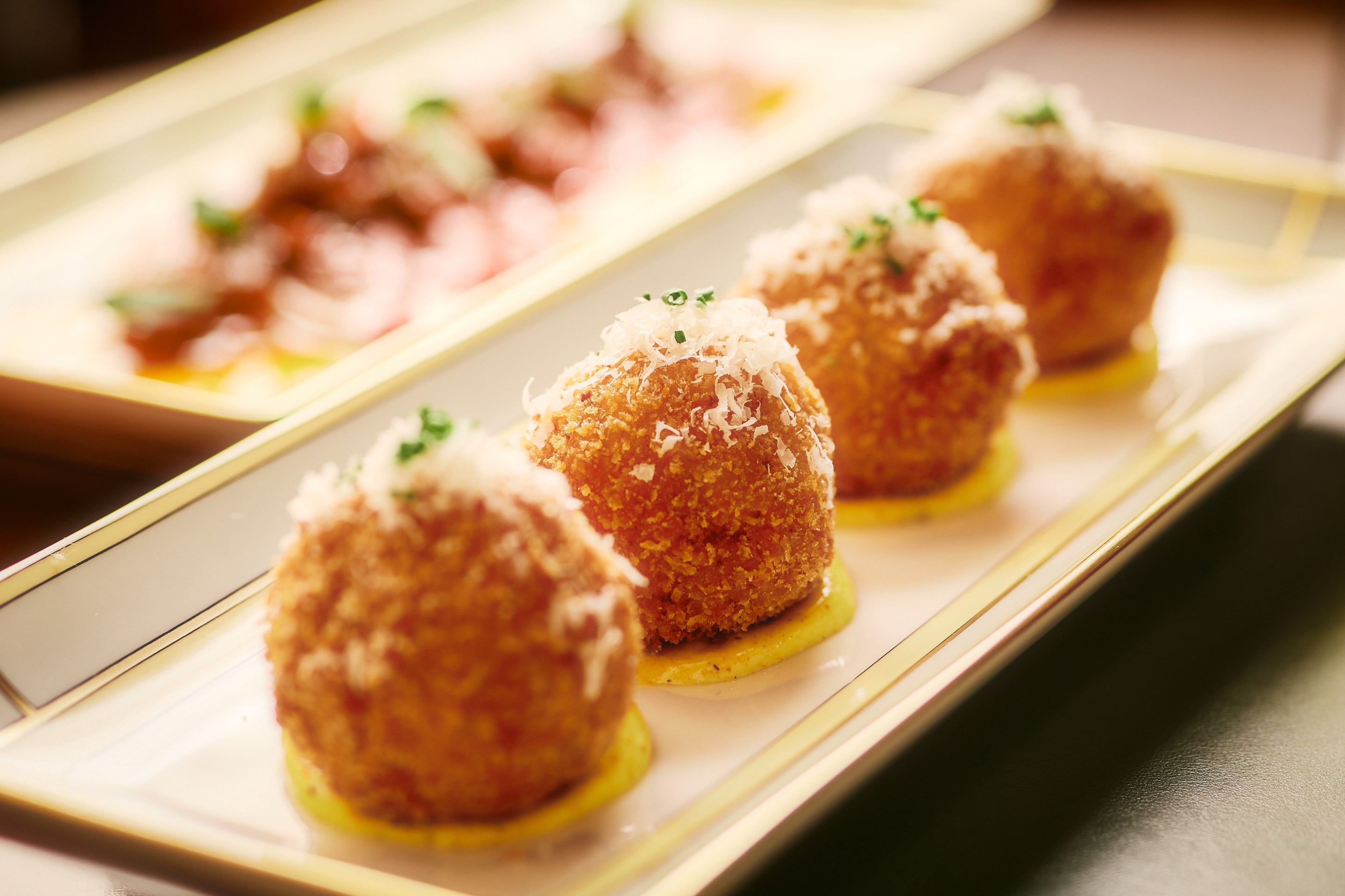 Golden lobster arancini topped with grated cheese and herbs, served on a white platter