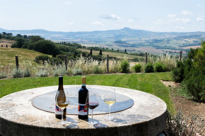 Wine bottles and glasses overlooking vineyards in Tuscany.