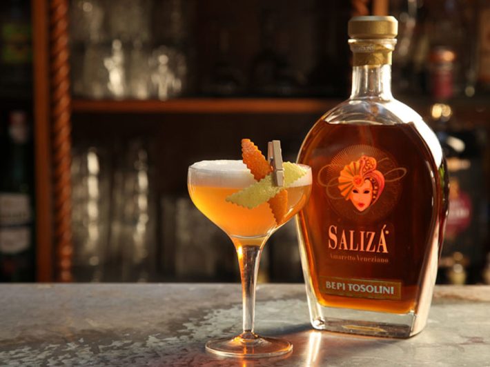 Bepi Tosolini Salizà Amaretto bottle beside an Amaretto Sour cocktail.