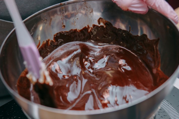 Cooking chocolate in a water bath. Hands black gloves are pink. Chocolate in an iron pan.