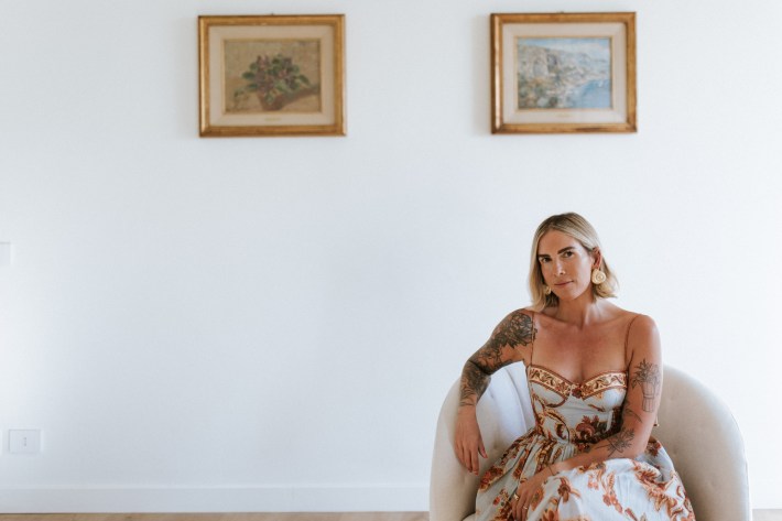 Kat Moore sitting in a white chair in her apartment in Ortigia