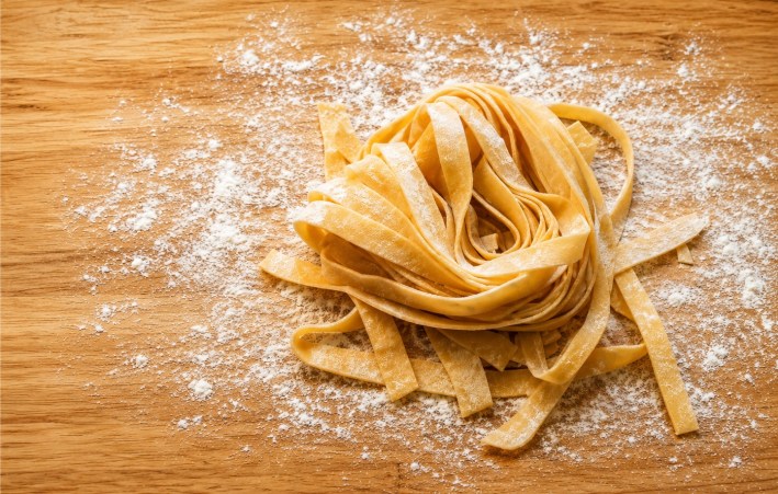 Fresh homemade fettuccine dusted with flour on a wooden surface.