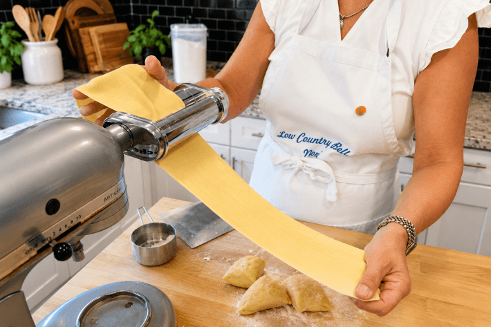 Fresh pasta dough being rolled through a pasta machine.