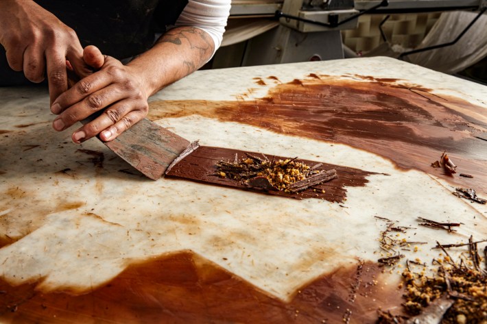 man chief collects cooled melted chocolate from marble tab