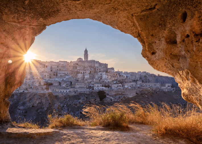 Matera, Italy, viewed through a large rocky cave opening at sunset.