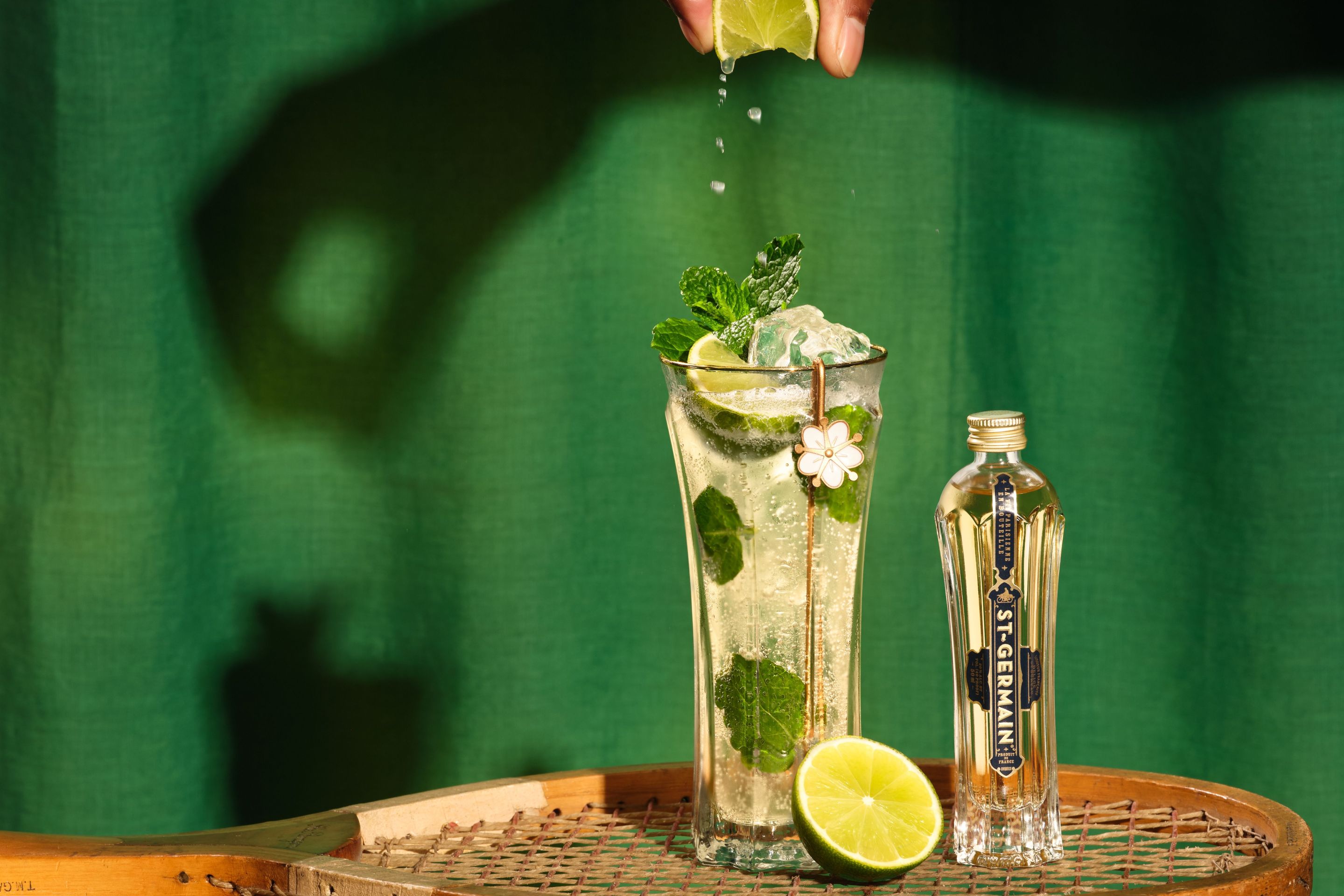 St-Germain Hugo Spritz with mint and lime beside a bottle of St-Germain Elderflower Liqueur.