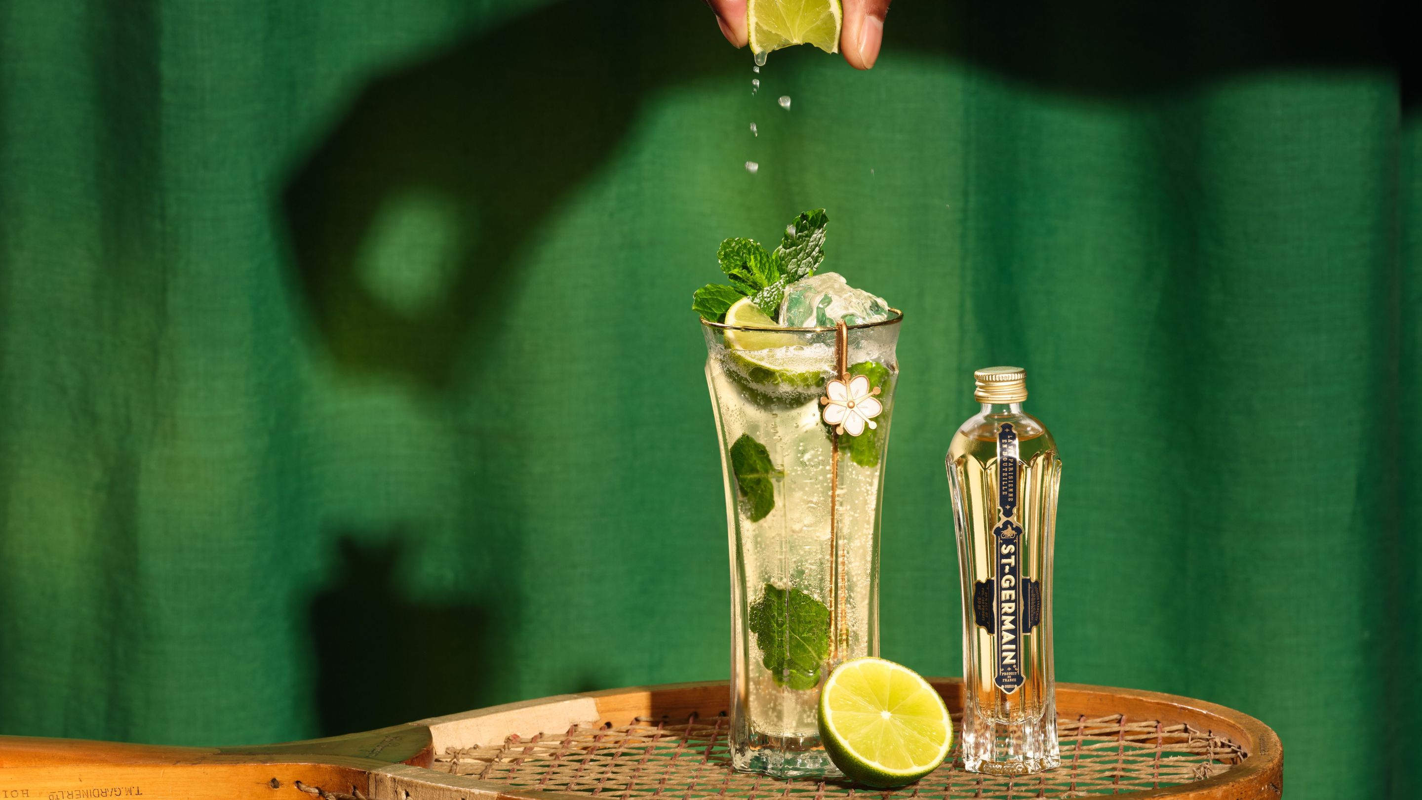 St-Germain Hugo Spritz with mint and lime beside a bottle of St-Germain Elderflower Liqueur.