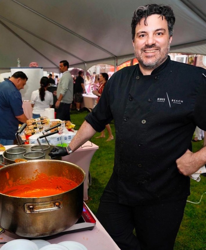 Chef Franco Vendome in a Nino’s Beach chef coat beside a large pot of tomato sauce.