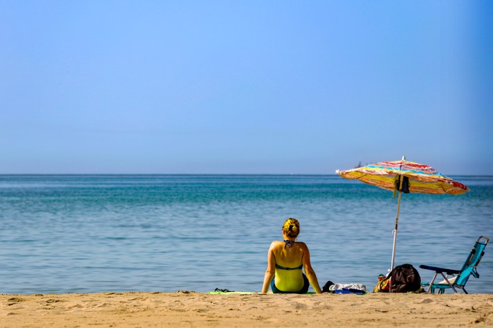 Woman relaxing on a beach with a chair and umbrella.