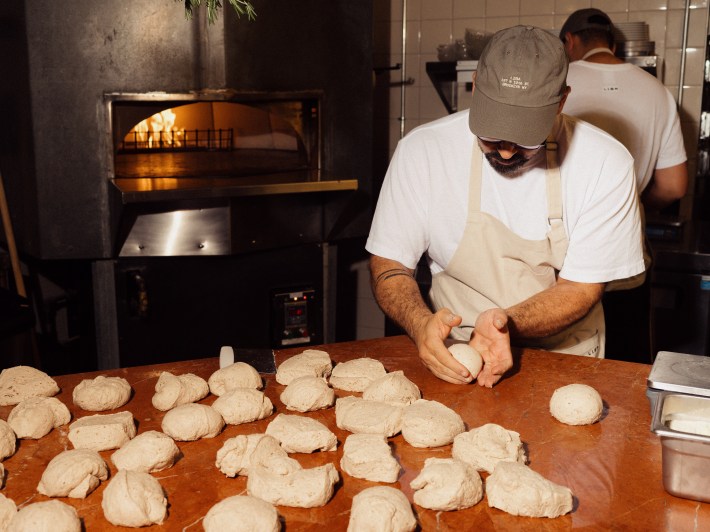 Chef shaping bread dough beside the brick oven at LIBA