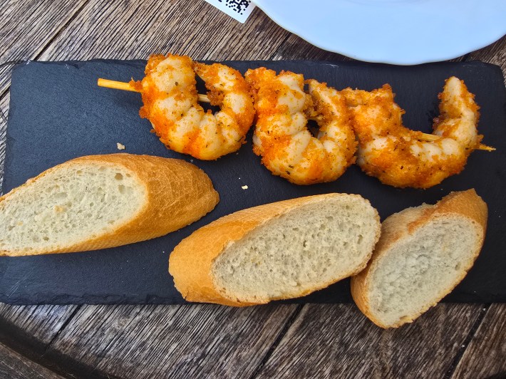 Prawn skewers and sliced bread on a black serving board.