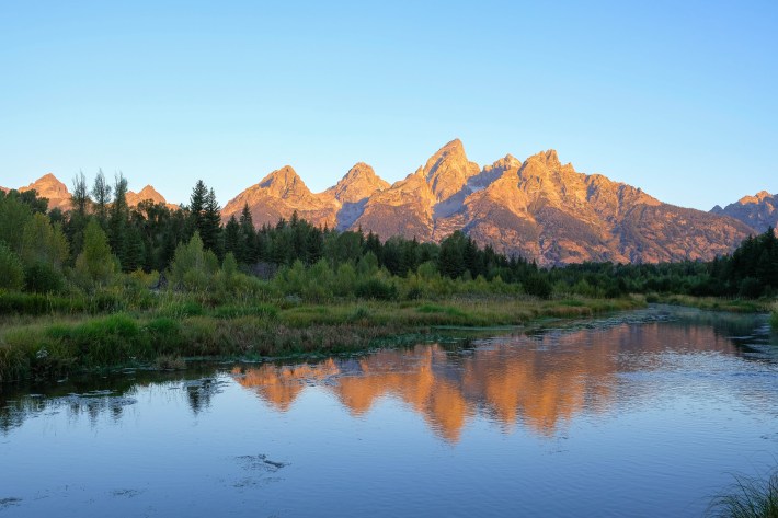 The Teton Range reflected in calm water at sunset.