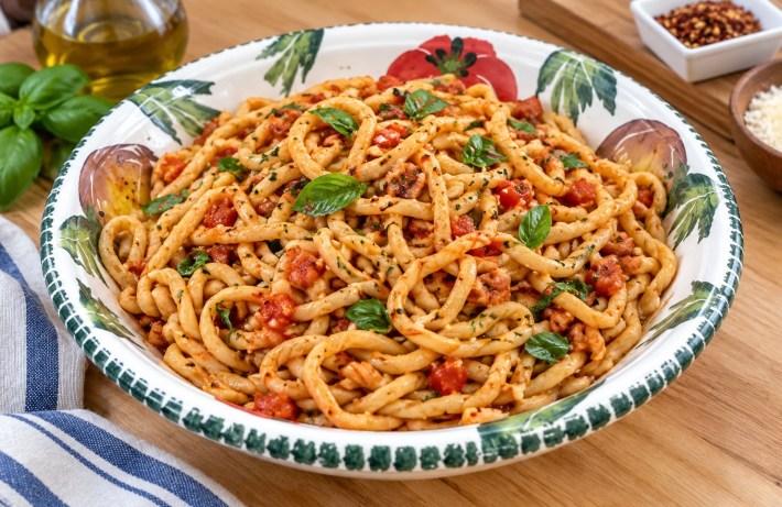 Bowl of handmade pici pasta with tomato sauce and basil