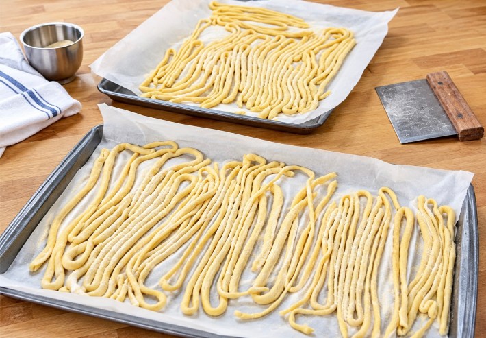 Handmade pici pasta strands on parchment-lined baking sheets