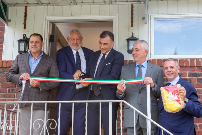 Five men stand outside a building as one cuts a green, white and red ribbon.