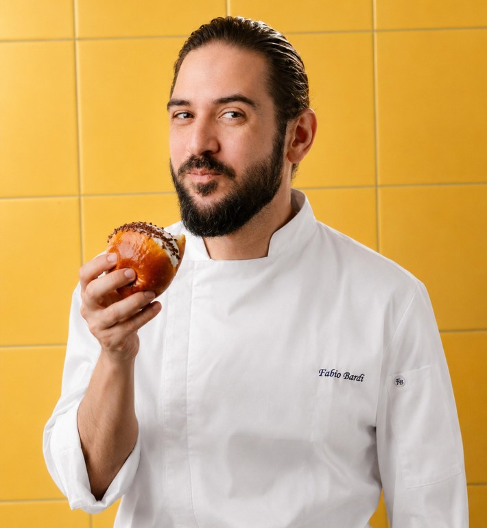 Chef Fabio Bardi holding a maritozzo with a yellow tiled background