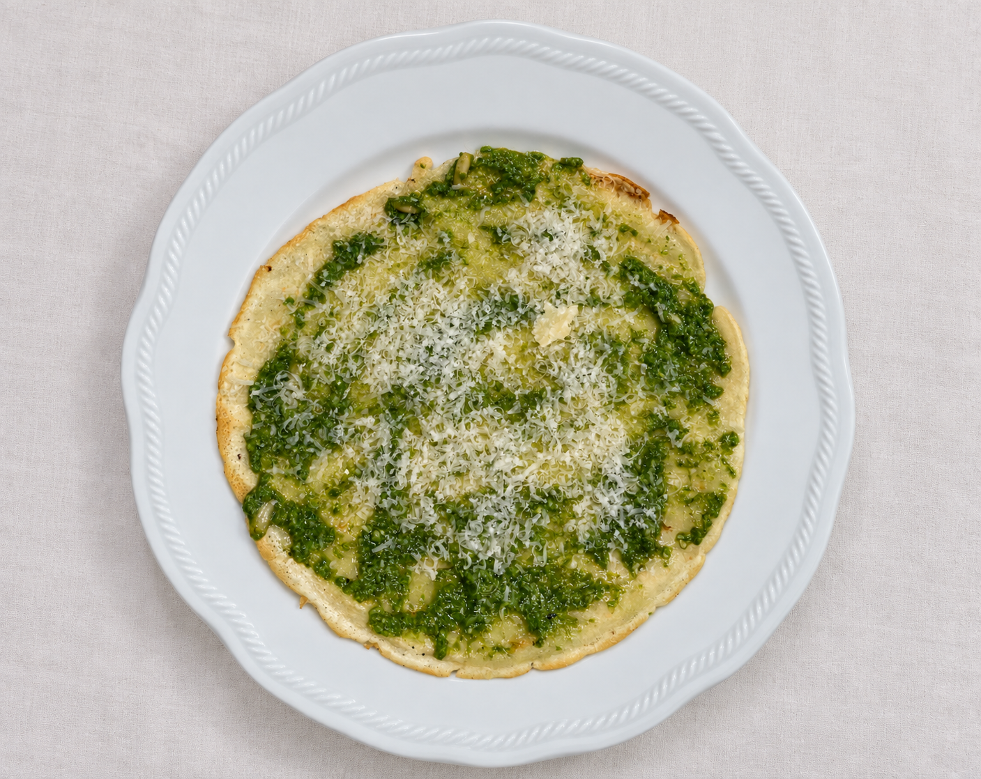 Ligurian testaroli with basil pesto and grated Parmigiano-Reggiano on a white plate.
