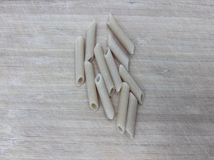 Dry penne pasta on a wooden surface