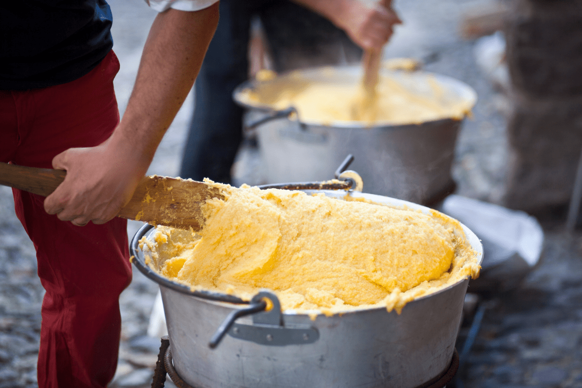 Polenta being stirred in large metal pots.
