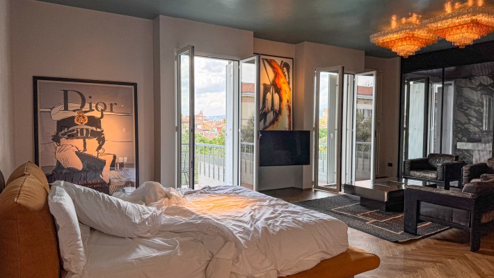 Hotel Trieste guest room with framed artwork, an amber chandelier, leather seating and open balcony doors.