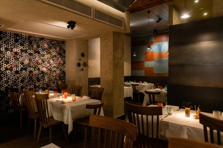 Locanda 4 Cuochi’s dining room with patterned walls, wooden chairs and colorful glasses on white-clothed tables.
