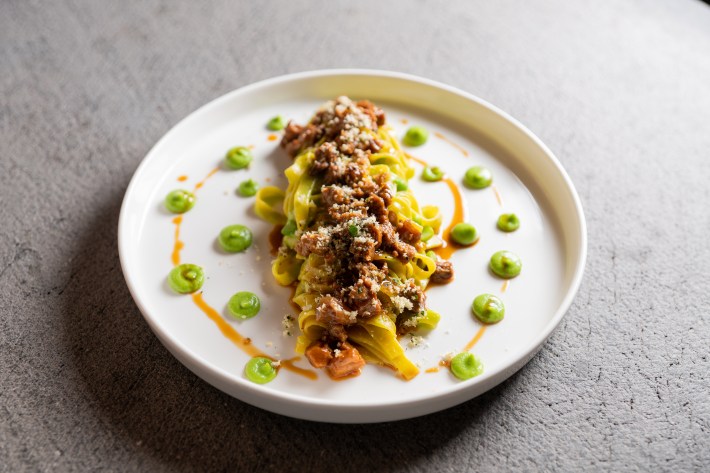 Tagliatelle topped with rabbit and chanterelle ragù, surrounded by dots of green pea puree on a white plate.