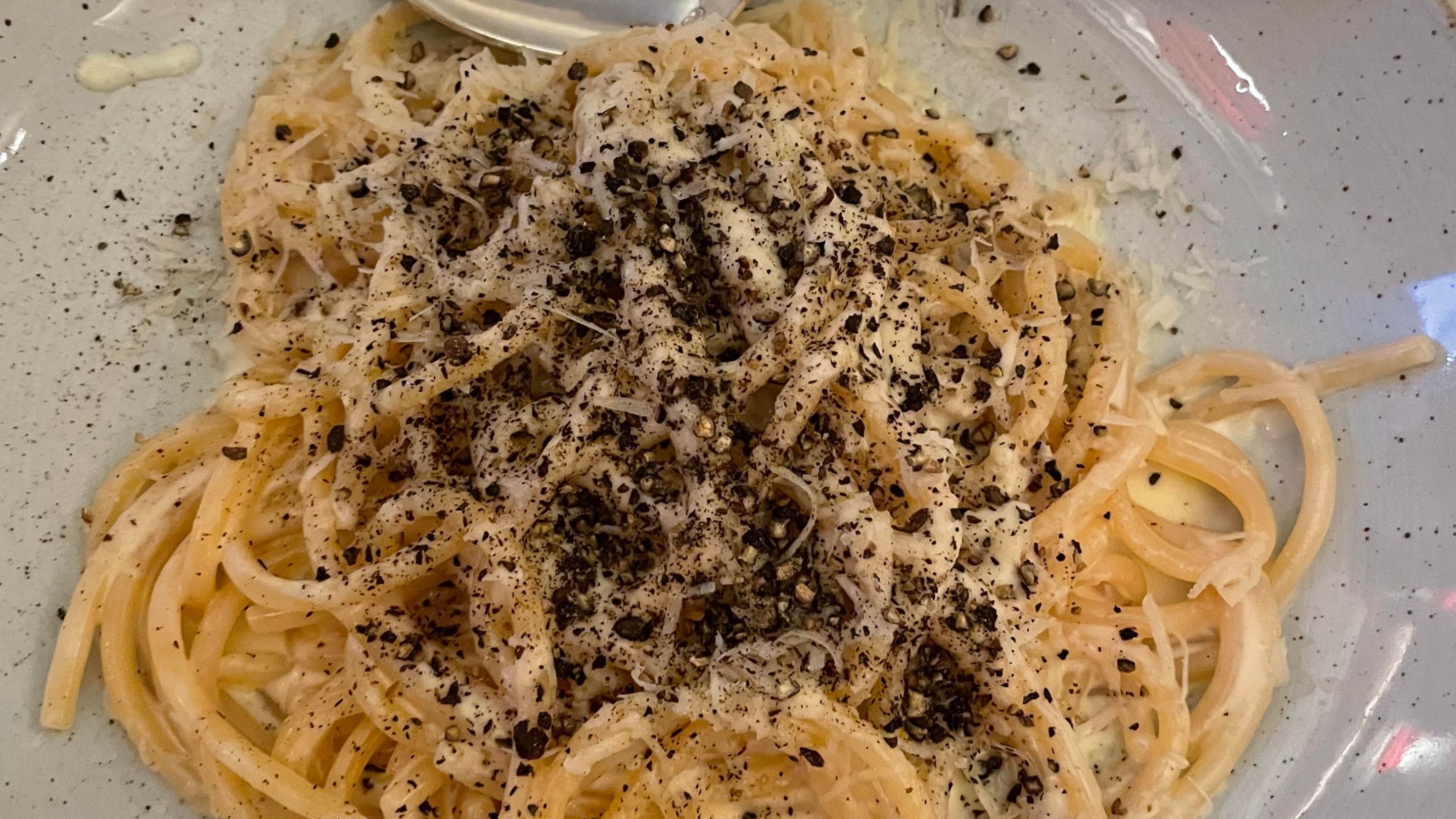 A bowl of cacio e pepe and a spoon.