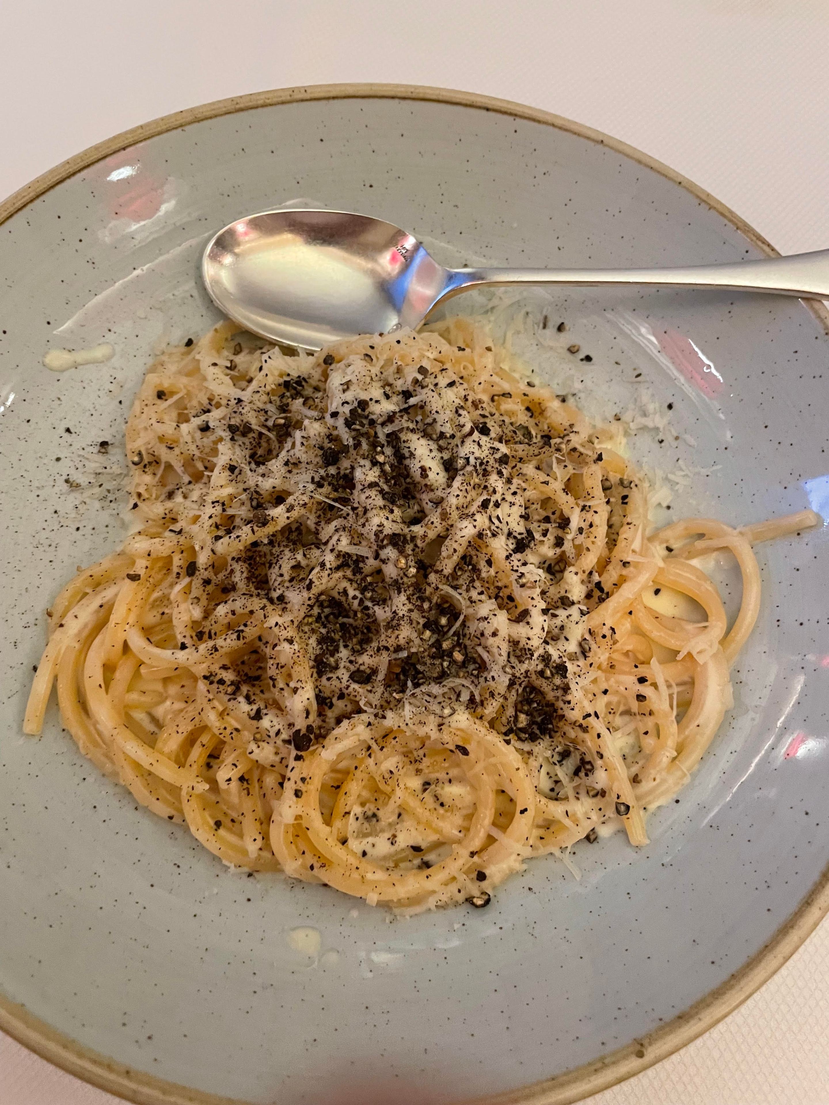 A bowl of cacio e pepe and a spoon.