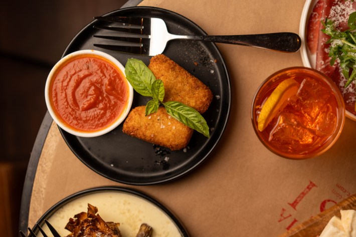 Two golden arancini with basil and a bowl of marinara on a black plate.