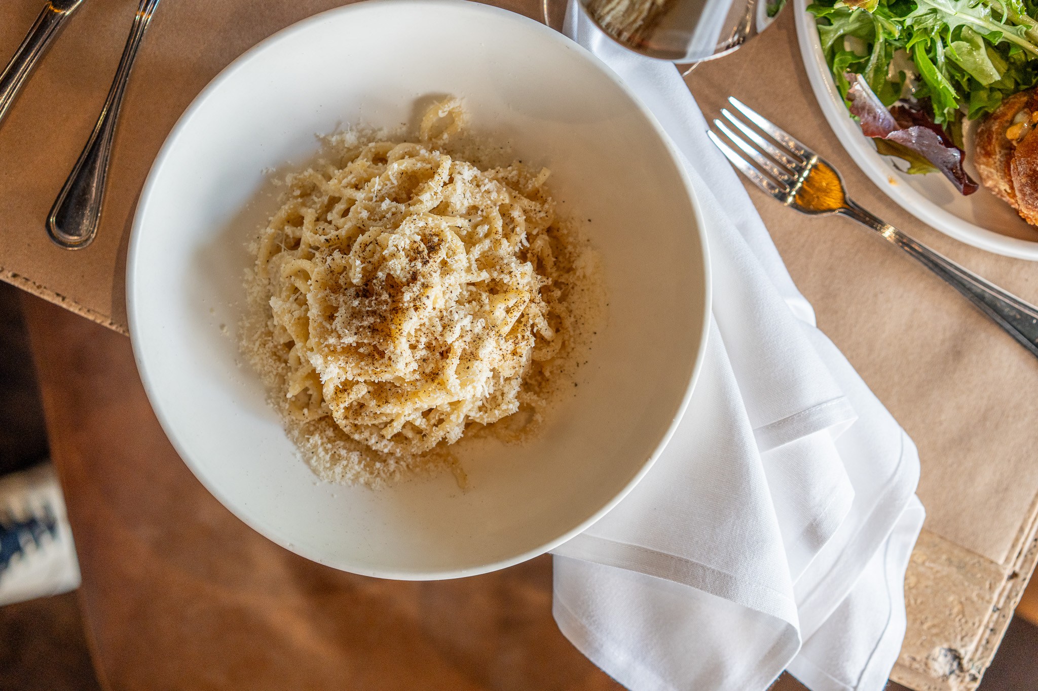 Cacio e pepe topped with grated cheese and black pepper in a white bowl.
