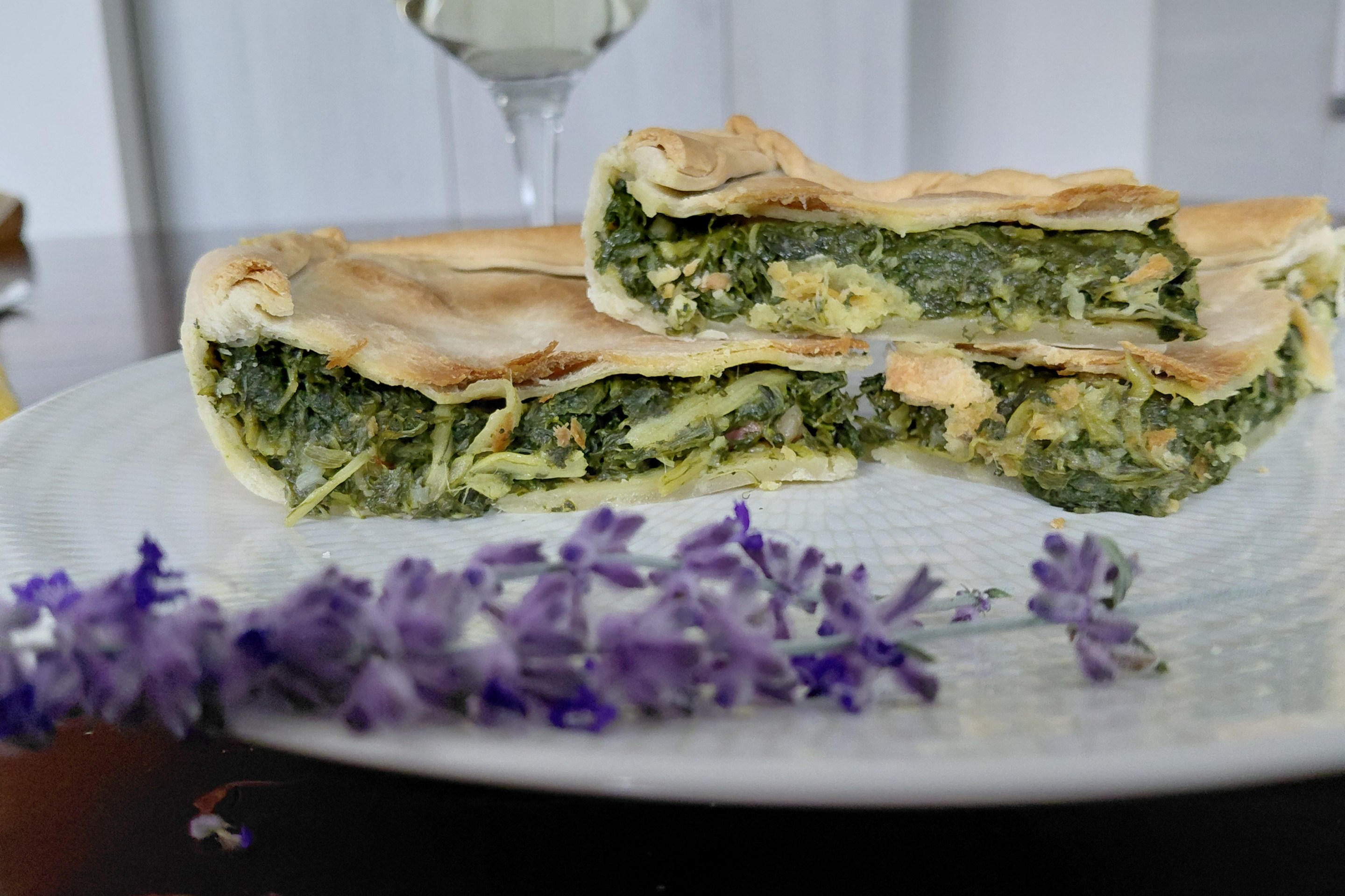 Slices of erbazzone with green filling on a white plate beside purple flowers.