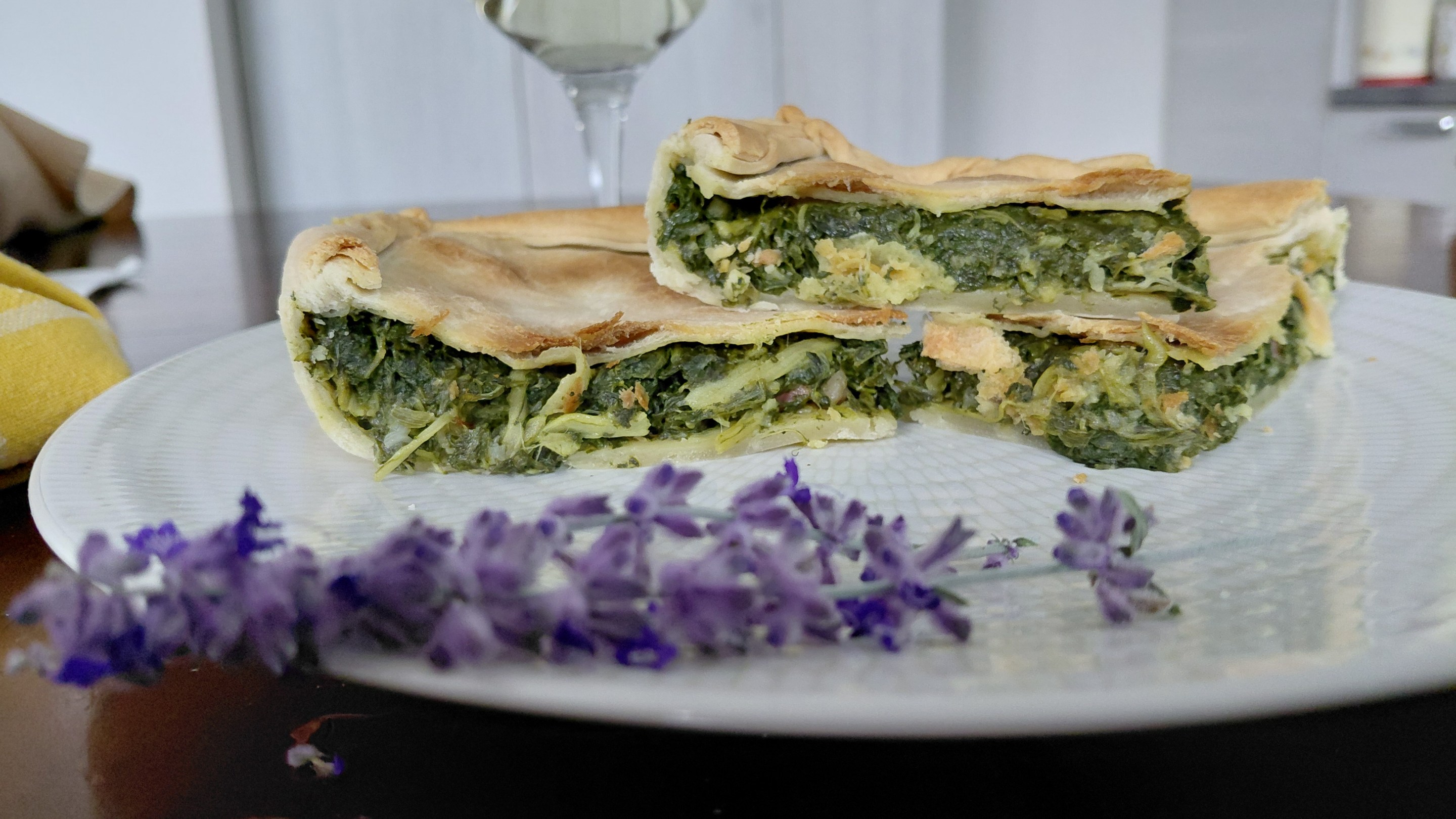 Slices of erbazzone with green filling on a white plate beside purple flowers.