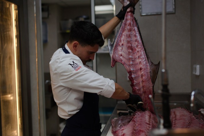 Chef Gennaro Liguori breaking down a large fish in a professional kitchen.