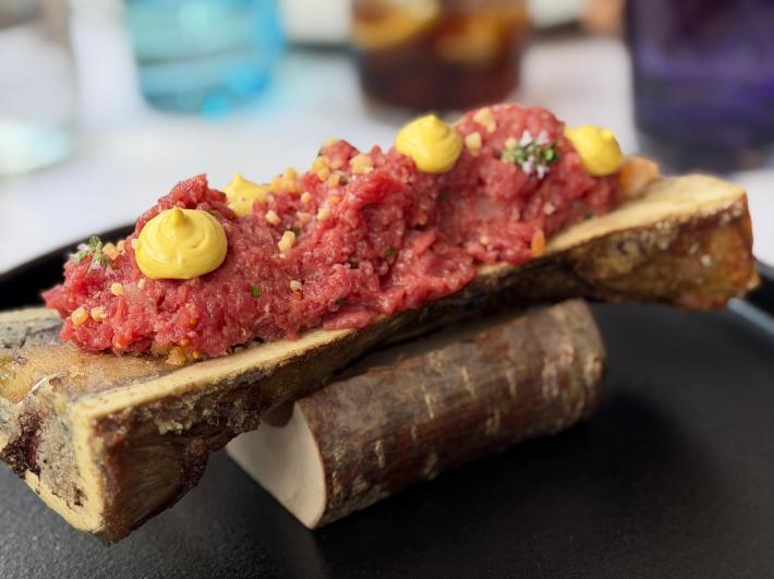 Beef tartare with yellow sauce and herbs served on a split marrow bone.