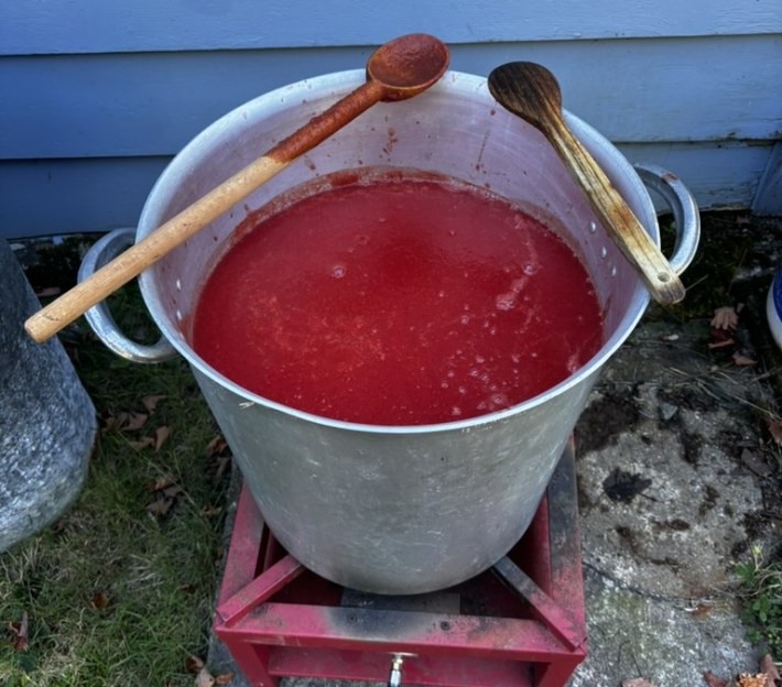 Red tomato sauce in a large metal pot with a wooden spoon across the rim