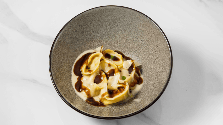 Cacio e pepe tortelli with sauce and cheese shavings in a gray bowl at Audace.